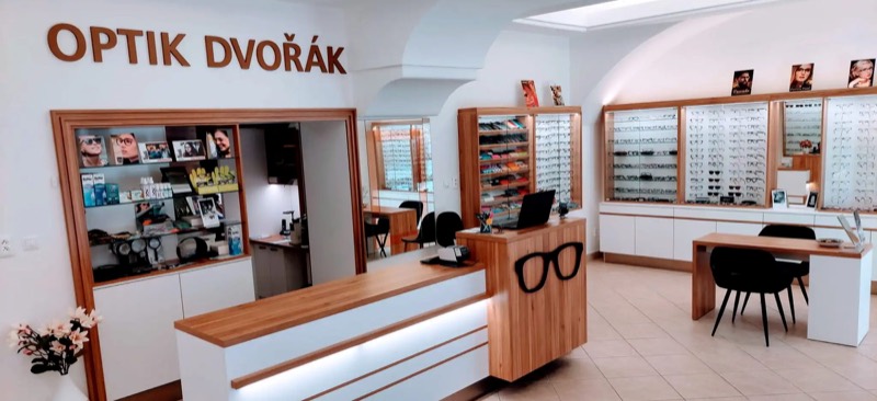 Interiér prodejny Optik Dvořák — dřevěné vitríny plné brýlových obrub, pult s logem brýlí a nápis OPTIK DVOŘÁK na stěně
