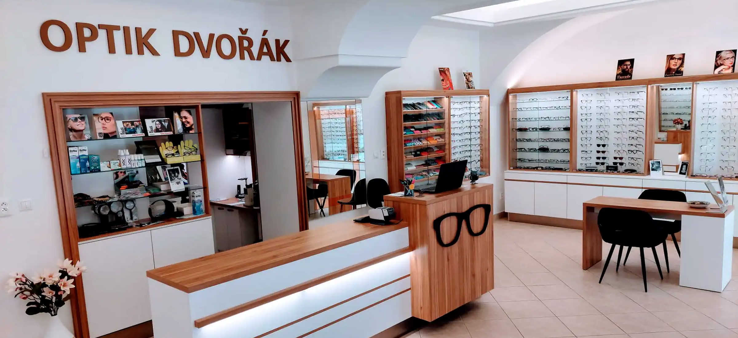 Interiér prodejny Optik Dvořák — dřevěné vitríny plné brýlových obrub, pult s logem brýlí a nápis OPTIK DVOŘÁK na stěně